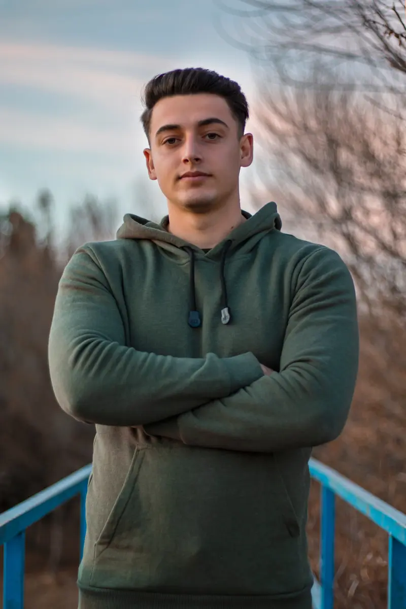 man in green hoodie standing on blue metal railings during daytime