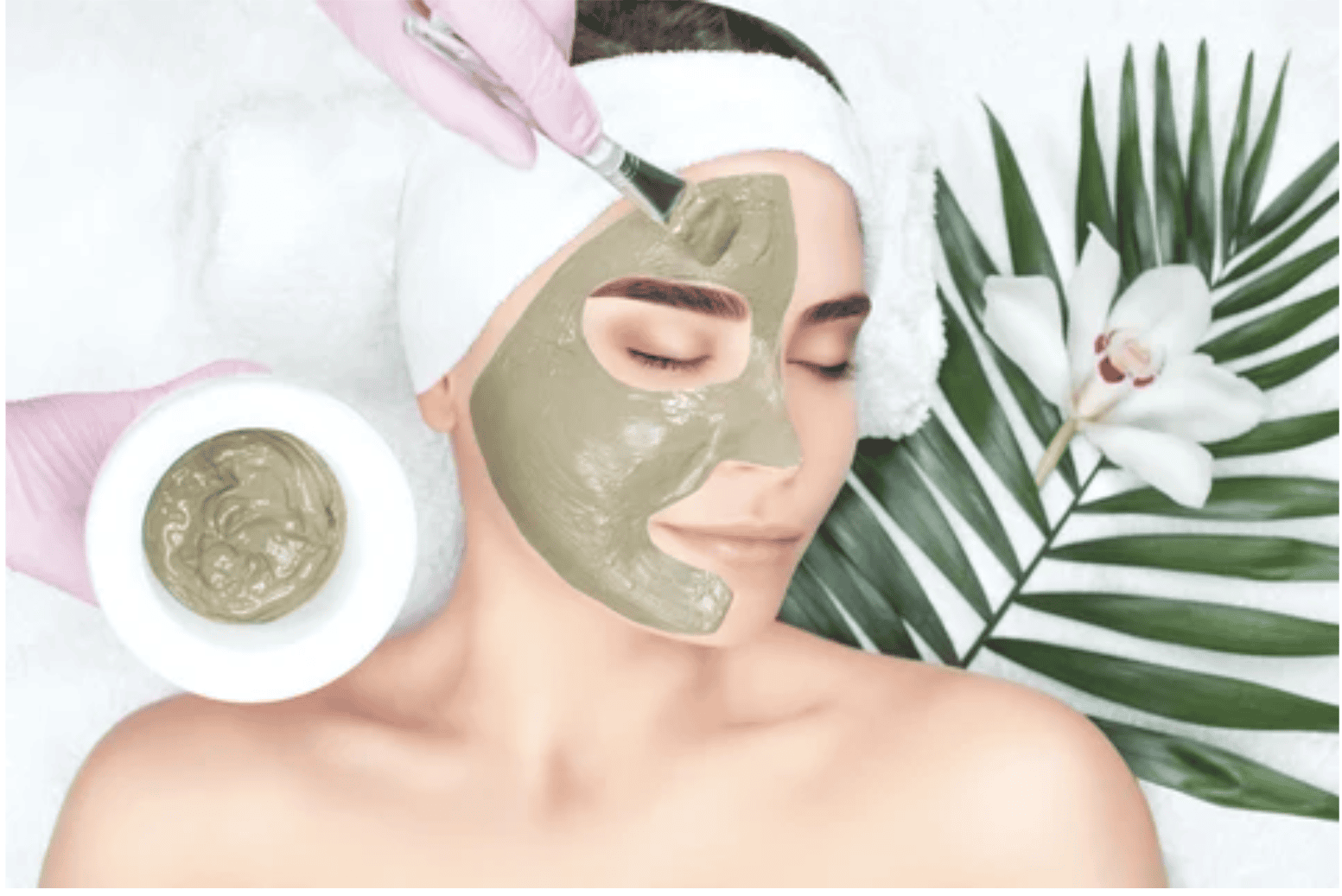 Harmony Hormone Solutions - Person lying on a spa bed receives a green facial mask applied with a brush. A green leaf and white orchid are placed beside their head.